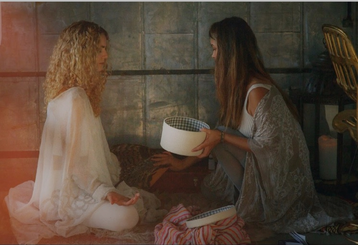 Sarah holding a singing bowl beside a seated participant