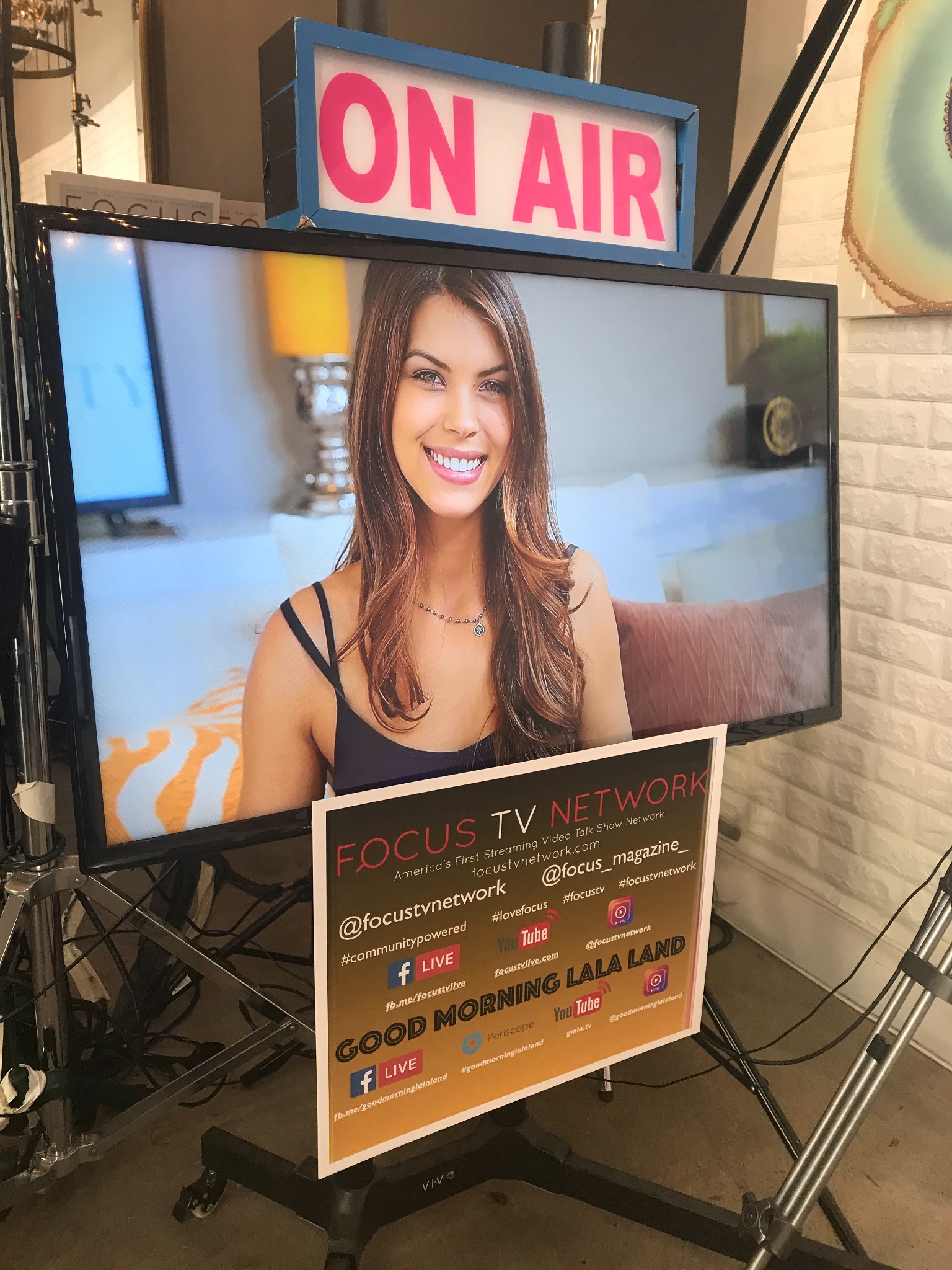 Sarah on a television studio monitor beneath an On Air sign