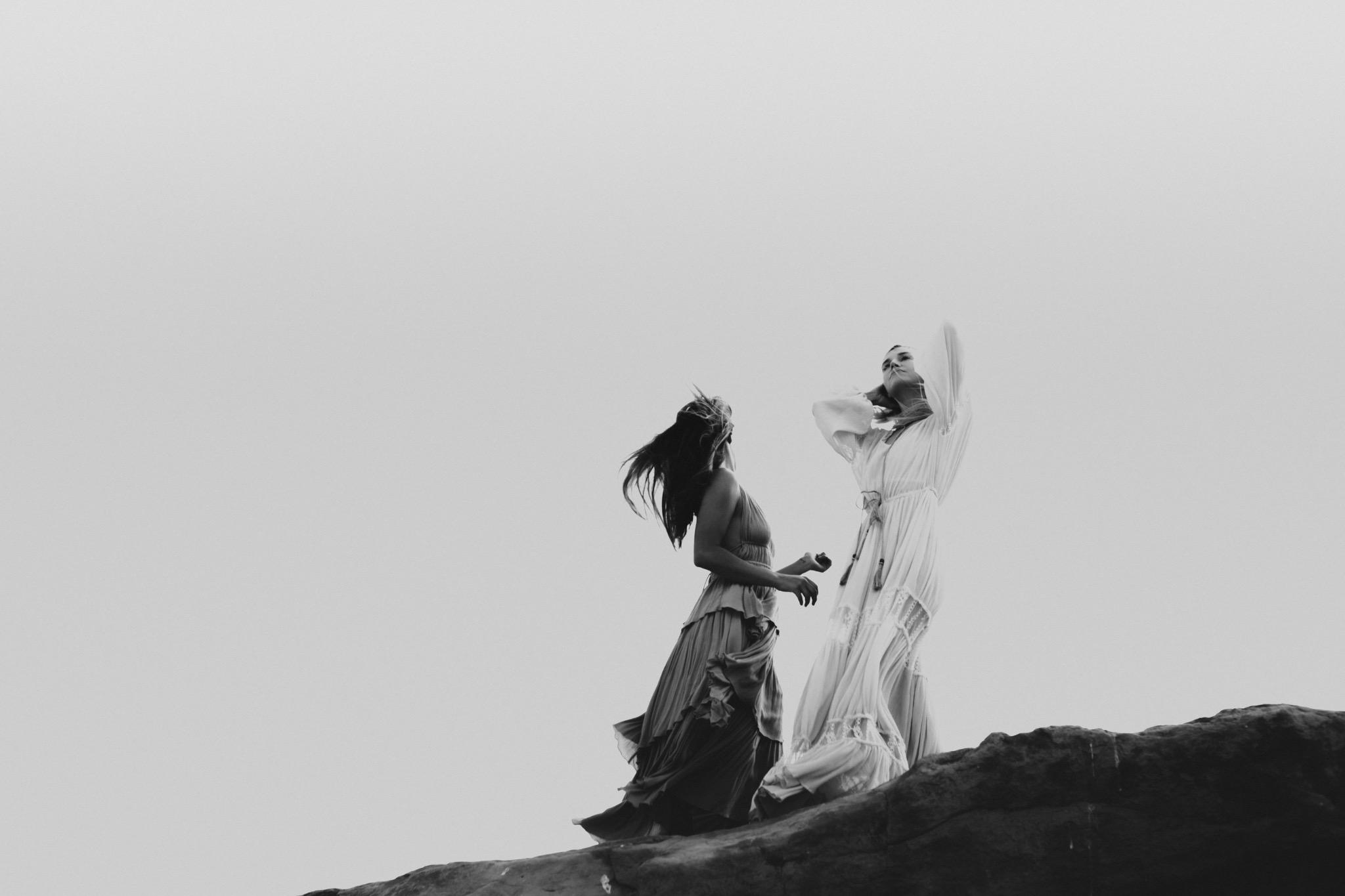 Two women standing on a rocky outcrop against an open sky
